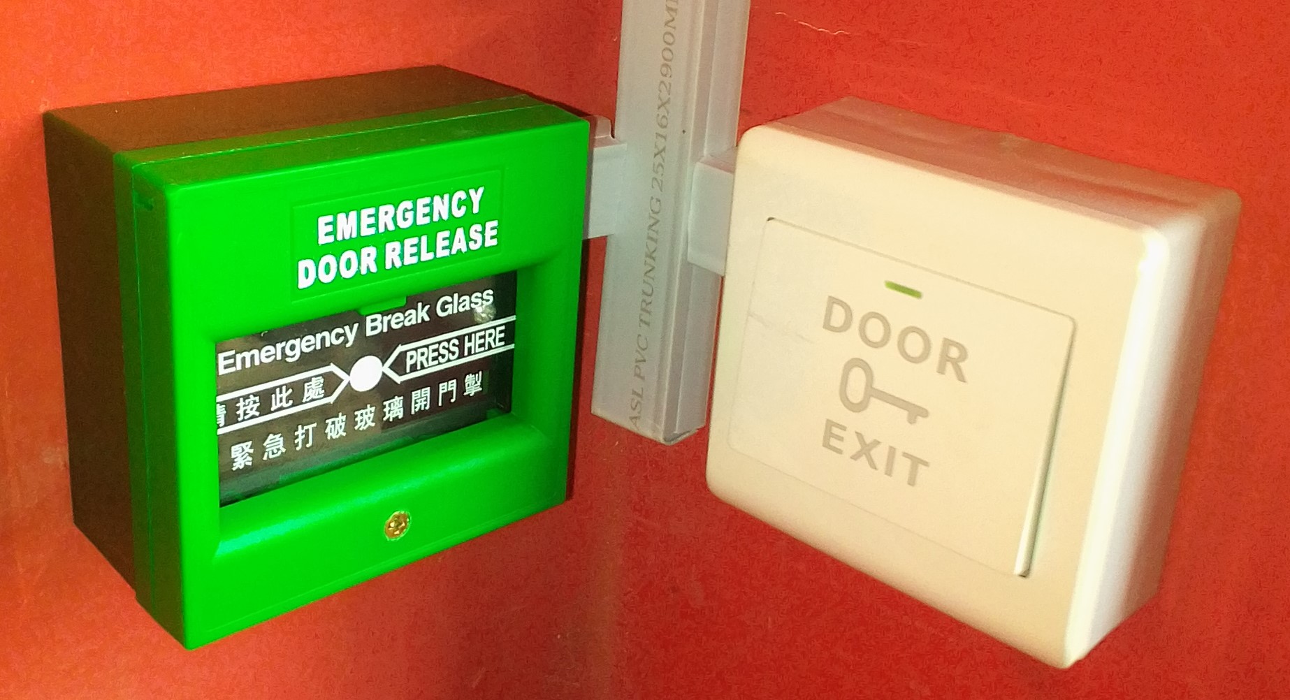 An emergency break glass (green) opens a door during an emergency or in case of a failed exit button (white) which is the one normally used for exiting.